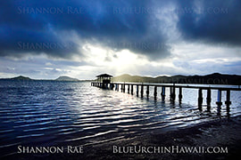 Stormy hawaii sunrise picture taken of an ocean pier as morning monsoon rain & clouds pass over 